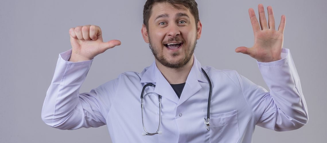 young man doctor wearing white coat and stethoscope showing number six with hand and fingers smiling over isolated white background